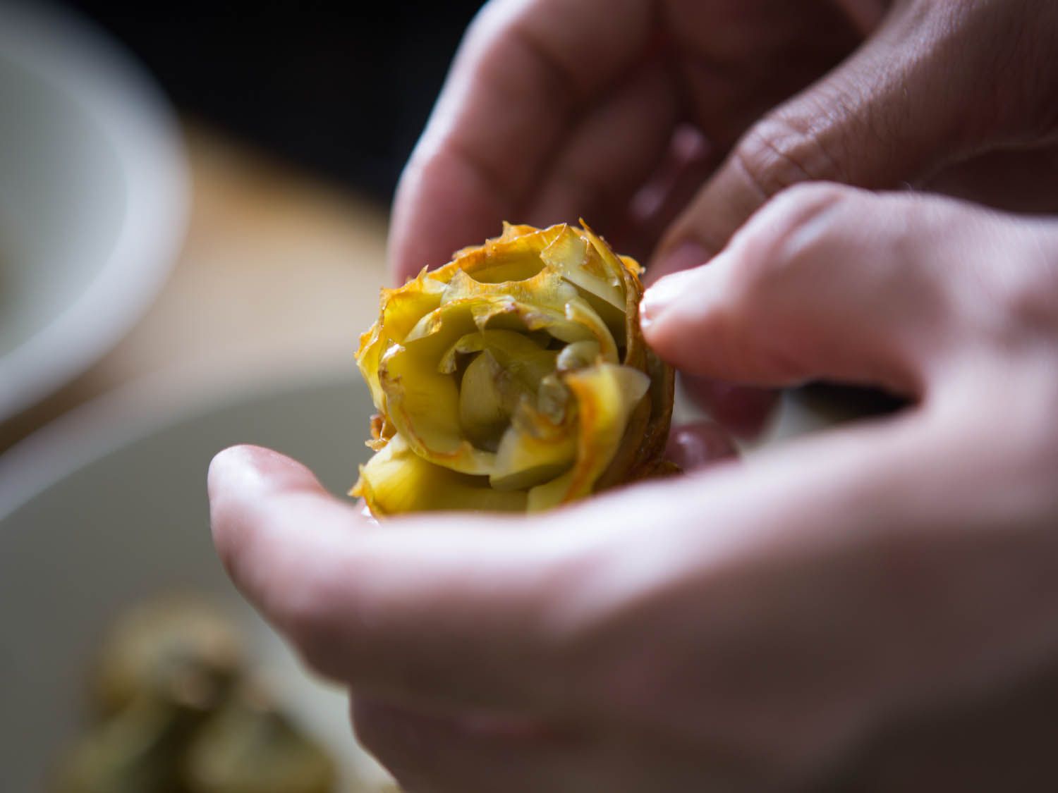 Close-up of hands gently prying open the leaves of fried artichoke heart.