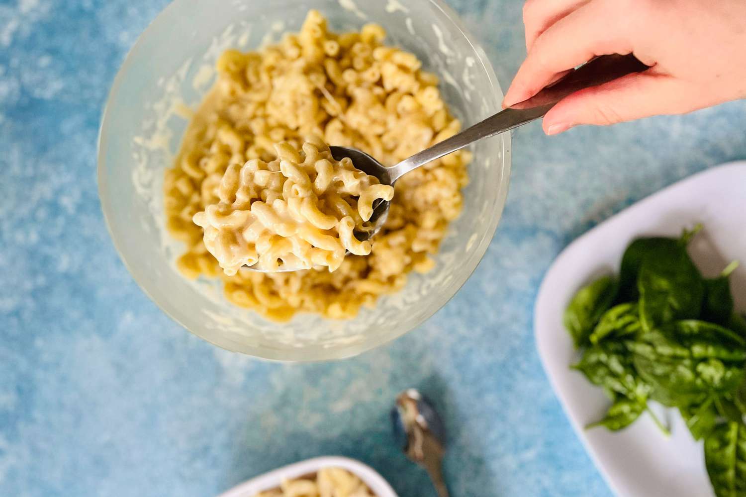 A hand holding a spoon and scooping macaroni and cheese out of an Anyday dish