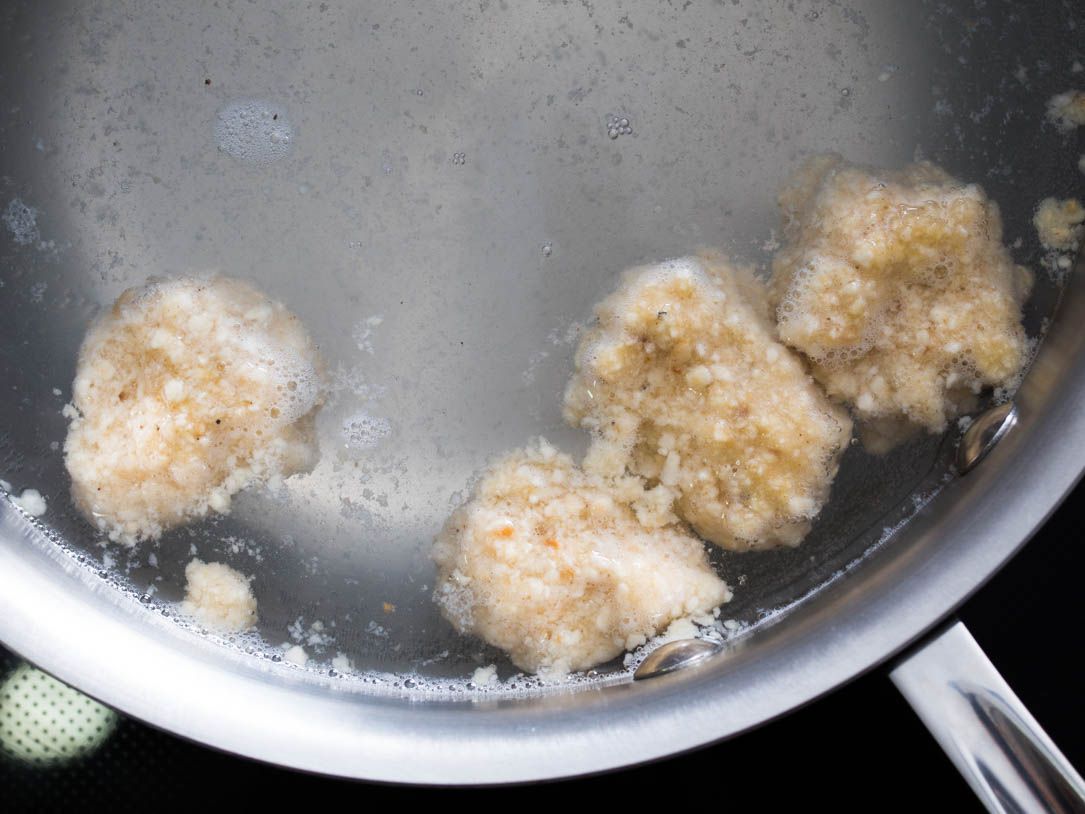 Fragments of matzo ball mixture floating in a pan filled with water.