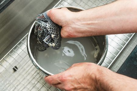 a hand using dough cloth to clean bread dough out of a bowl in a kitchen sink