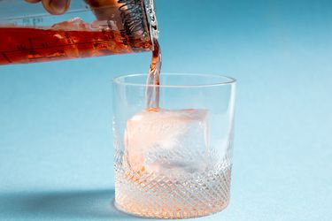 a cocktail being poured over a large ice cube in a rocks glass