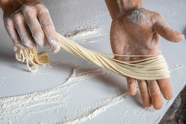 Hands holding thin hand-pulled lamian noodles over floured counter.