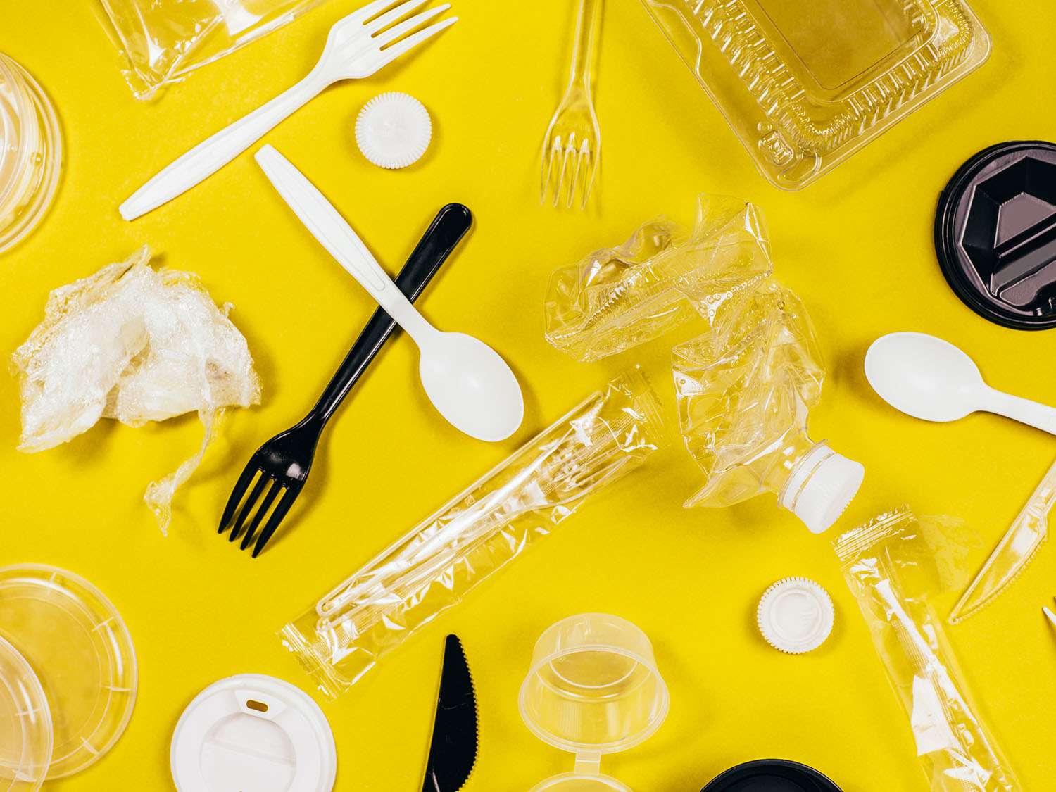 plastic spoons, forks, food containers, wrappers, and bottles on a yellow background