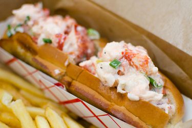 Lobster rolls in a basket next to some French fries.