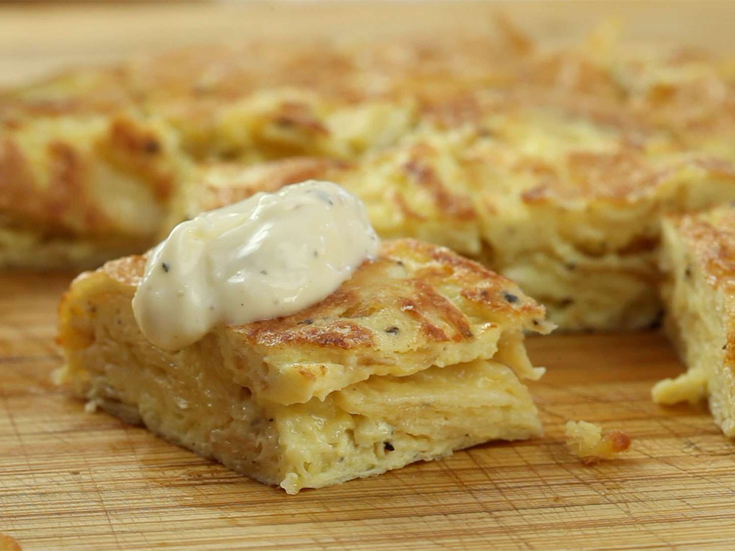 A cut piece of salt-and-vinegar Spanish tortilla topped with allioli