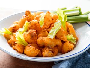 A plate of crispy buffalo fried cauliflower, with celery sticks on the side of the plate.