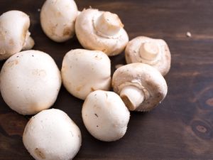 White button mushrooms piled on a wooden cutting board.