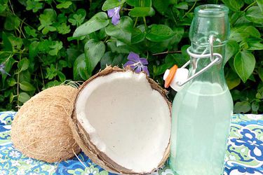 Fresh whole coconut cracked in half beside a bottle of homemade coconut rum