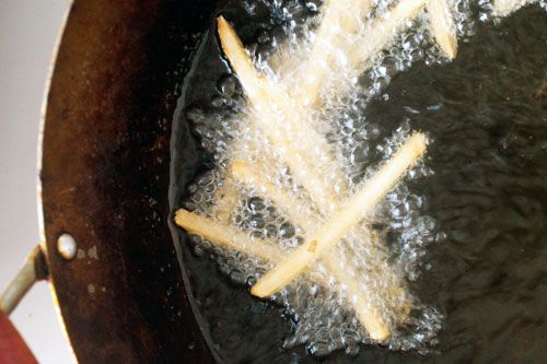French fries frying in hot oil in a pan. The oil is bubbling around the fries.