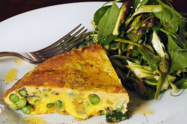 一片asparagus-sweet豌豆frittata, served on a plate with a minty spring salad.