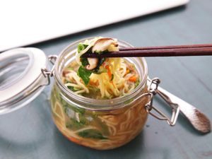 A clip top jar full of homemade instant noodles. A pair of chopsticks lifts a bite from the jar.