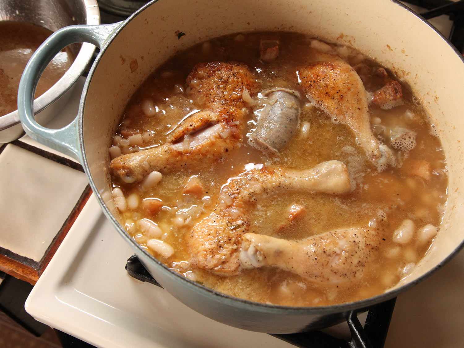 Beans, chicken, and sausages simmering in a Dutch oven.