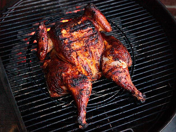 一只蝴蝶鸡放置在一个水壶式烤架的中心。深焦的表皮上涂满了烧烤酱。
