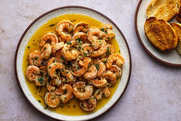 A plate of Spanish-Style Garlic Shrimp (Gambas al Ajillo). On the right hand side of the image is a smaller plate of toasted bread.