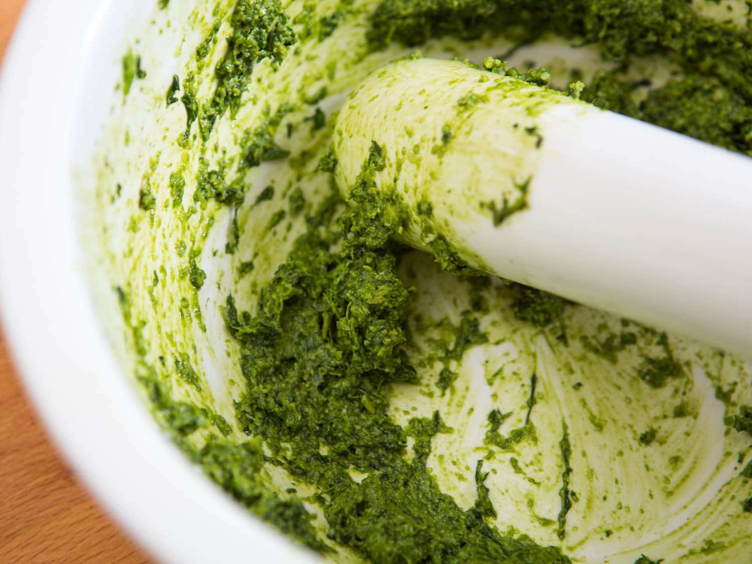 Closeup of pesto alla genovese being made with a marble mortar and pestle.