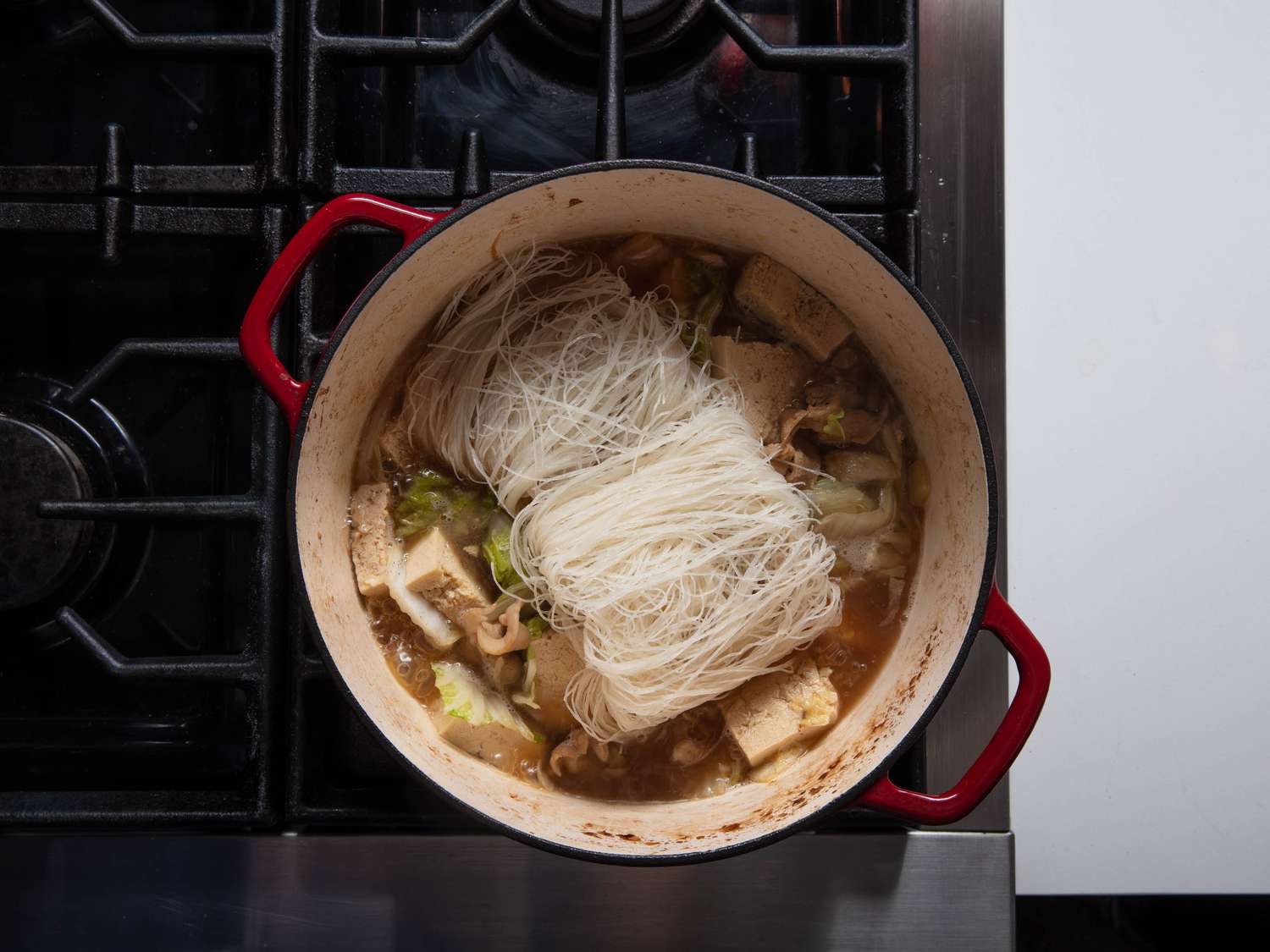 Soaked rice noodles on top of other contents of Dutch oven.