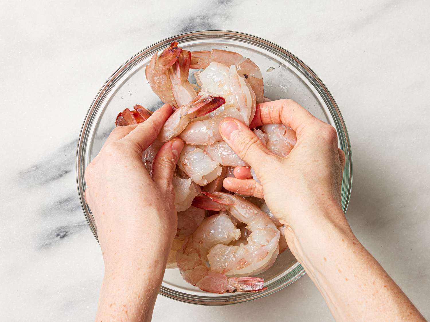 Shrimp in a glass bowl being tossed with kosher salt and baking soda.