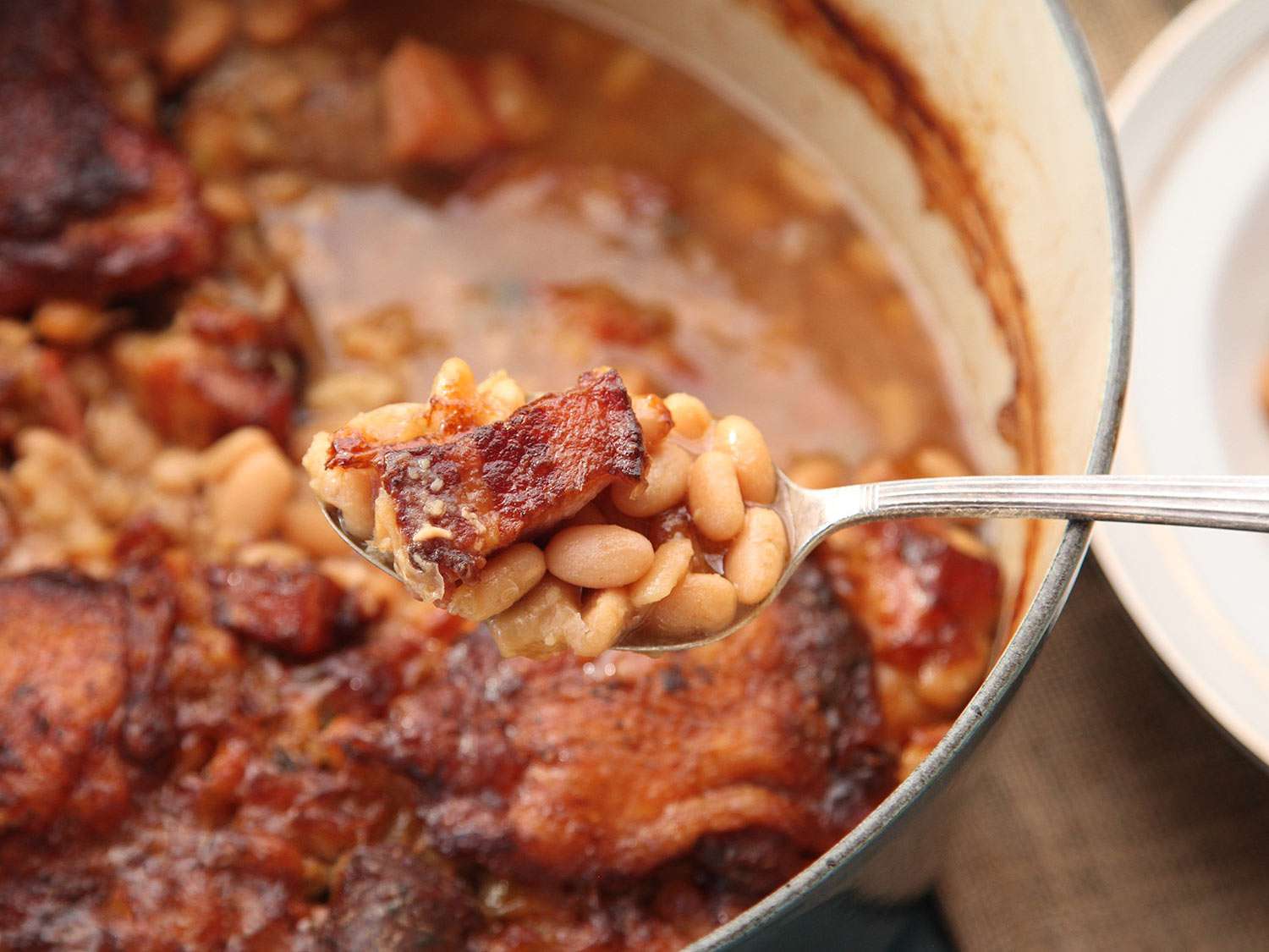 A spoon of tender beans and brown salt pork from the finished cassoulet with crisp skin.