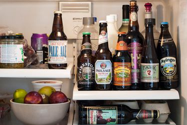 Seven different bottles of beer in a refrigerator. Six are all on one shelf with the labels facing out.