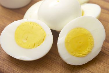 煮熟的鸡蛋放在木板上。一个鸡蛋切成两半，露出里面的蛋黄。