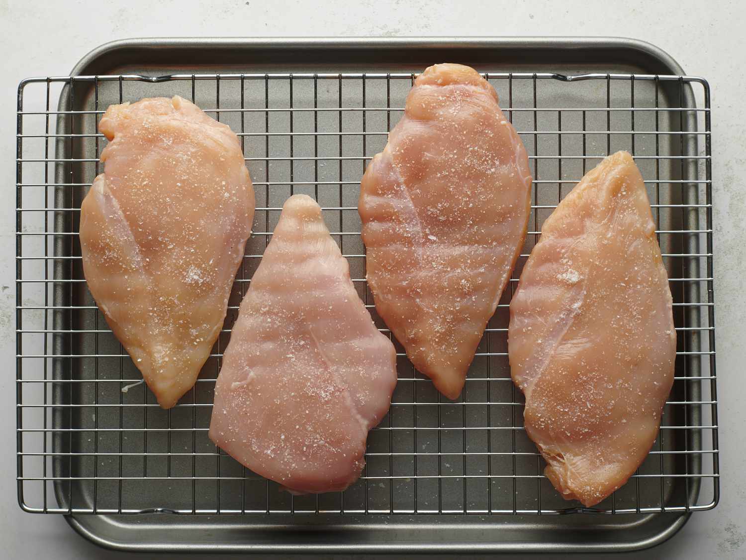 四个去骨去皮的鸡胸肉放在铁丝架上，放在一个小烤盘上。鸡胸肉已经被捣碎得有点平，撒上盐，表明它们是干卤水。gydF4y2Ba
