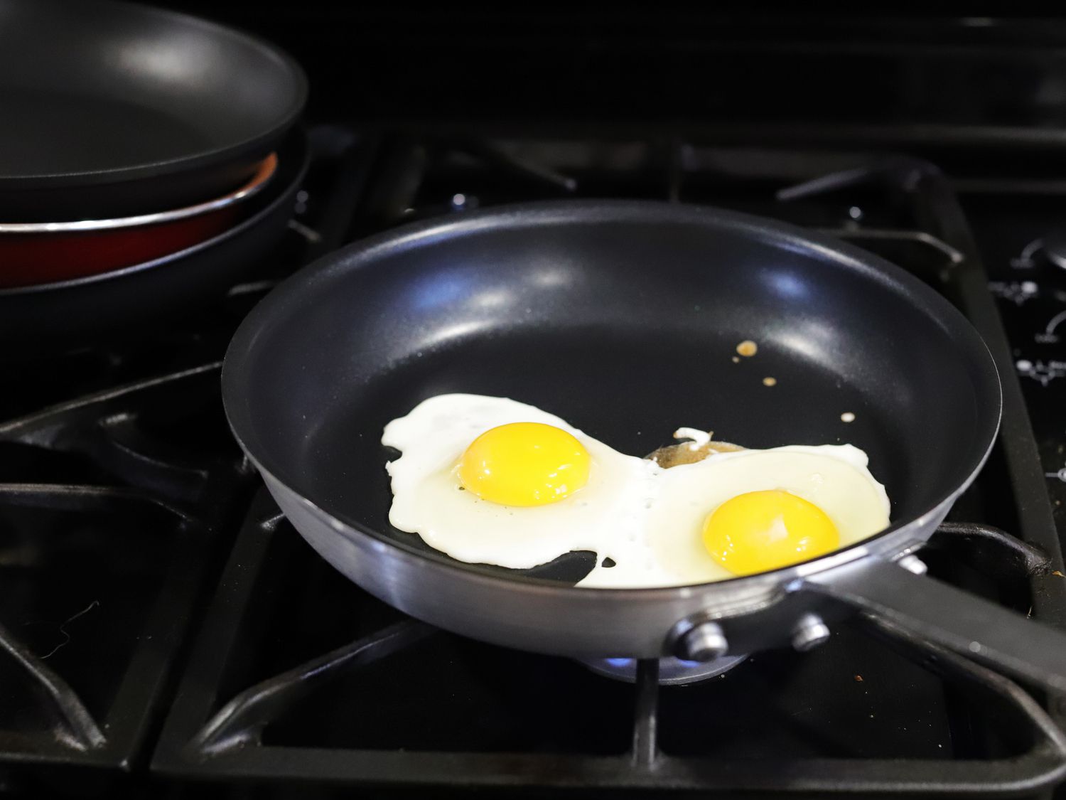 two eggs frying in a nonstick skillet on a gas stovetop