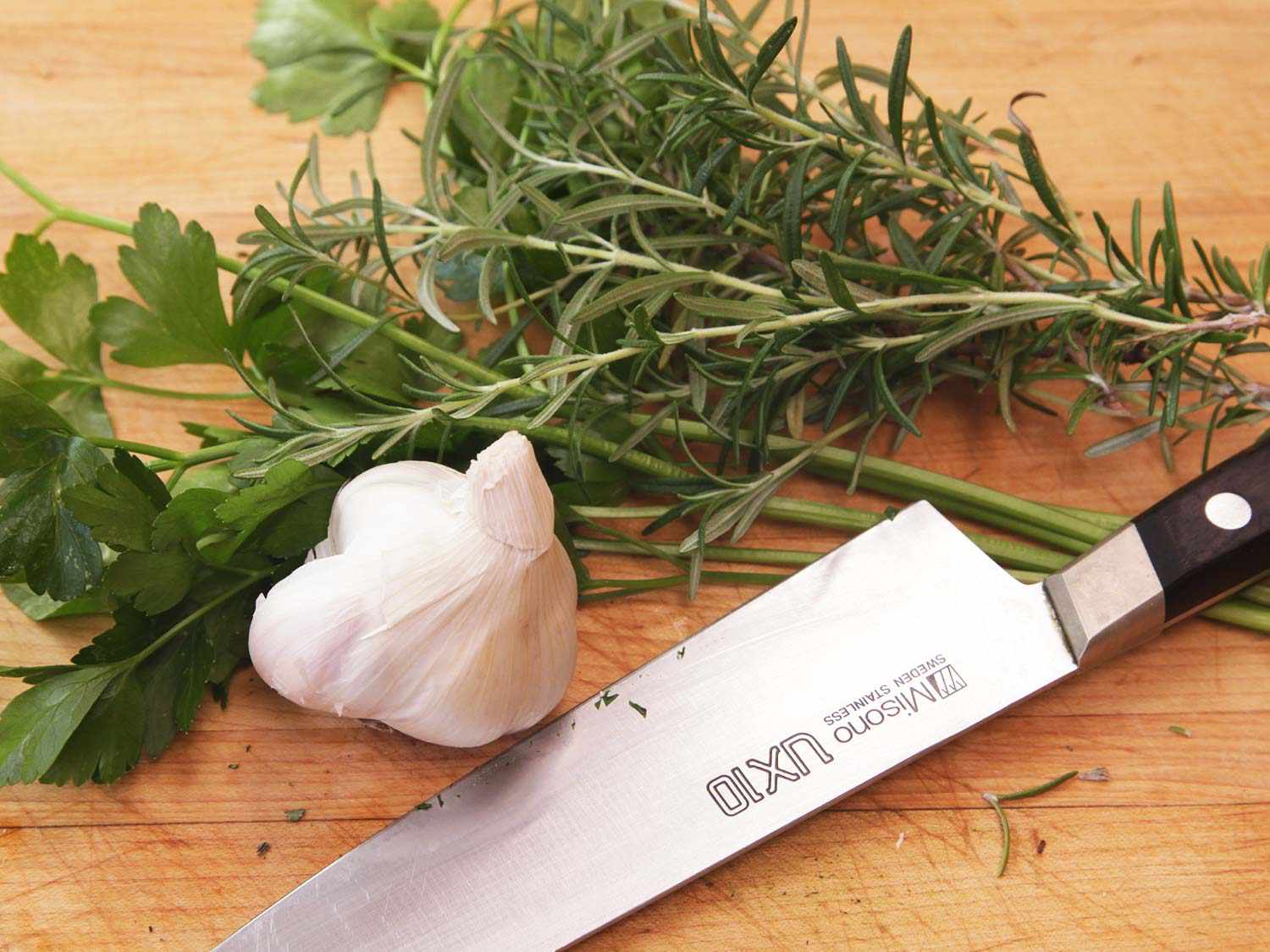把香芹、迷迭香和大蒜放在砧板上，放在刀旁边。