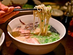 A bowl of ramen. Someone is using chopsticks to lift noodles above the bowl.