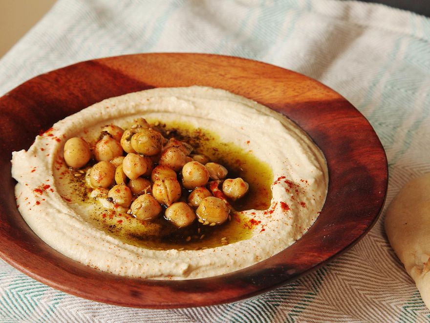 用浅木碗盛上奶油味的以色列式鹰嘴豆泥，上面撒上煮熟的鹰嘴豆、橄榄油、扎塔尔和辣椒粉。