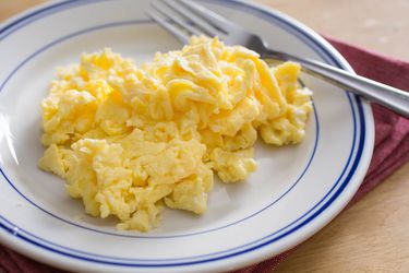 一个白蓝相间的盘子，上面放着一堆松软的炒鸡蛋，还有一把叉子。