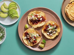 overhead view of three chorizo tacos flanked by plates of sliced avocado and charred corn tortillas