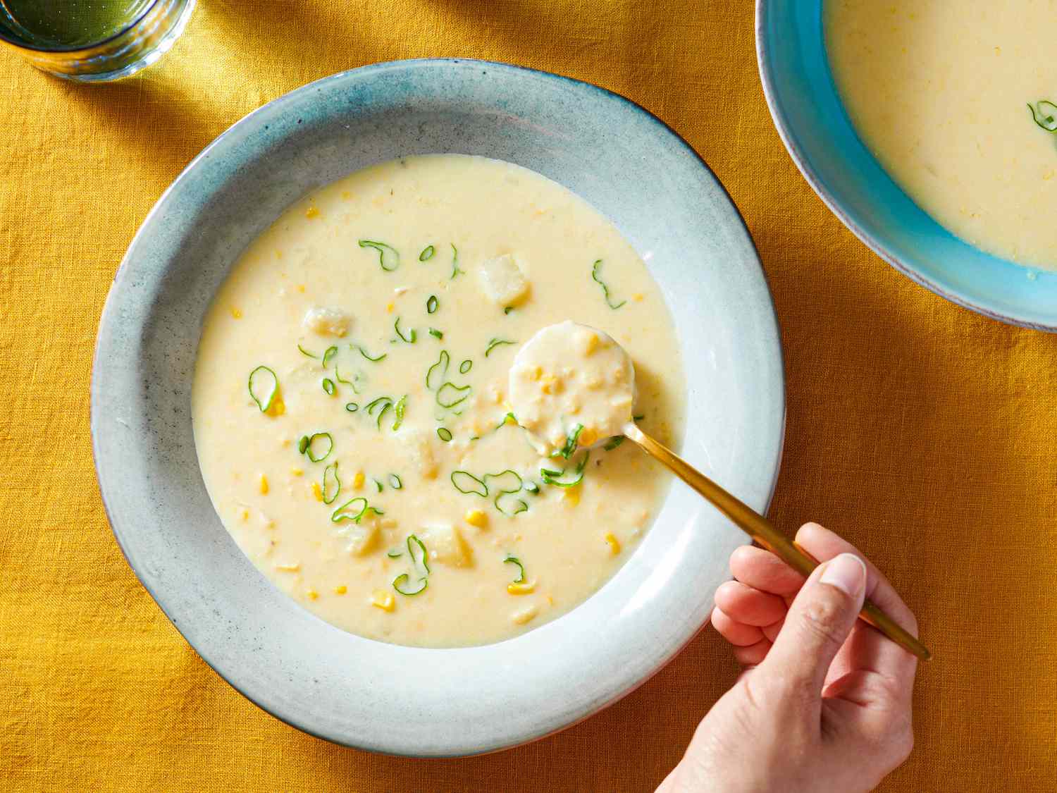 Corn chowder served inside a soup plate, sprinkled with sliced scallions