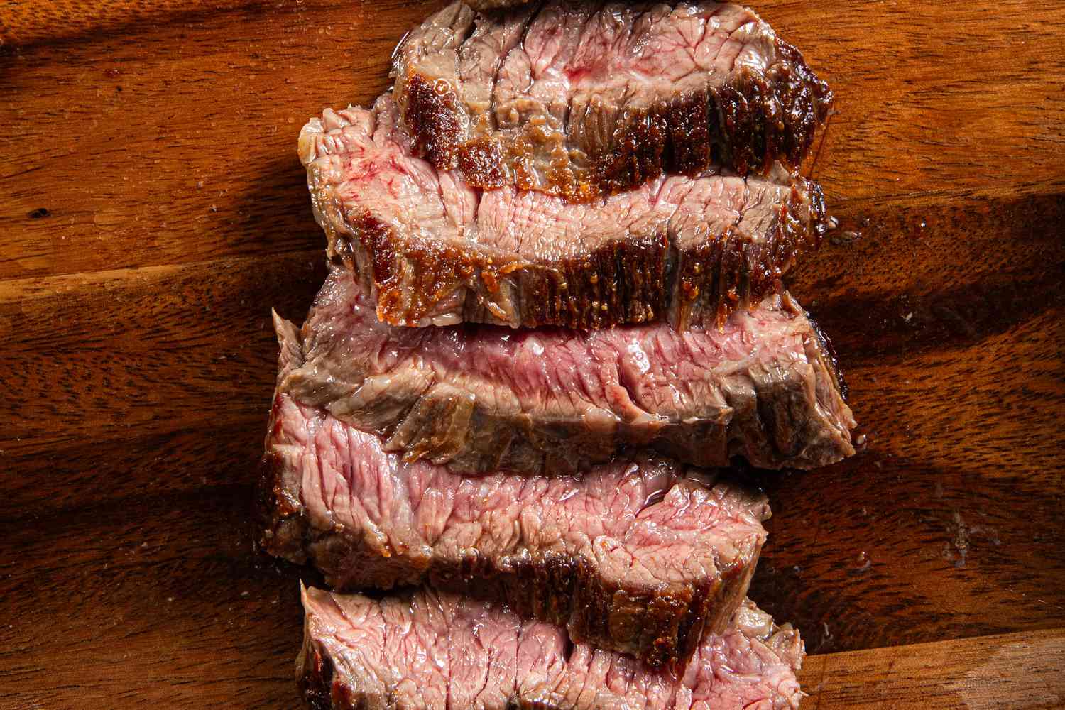 A piece of medium-rare steak sliced into thin pieces on a wooden cutting board.