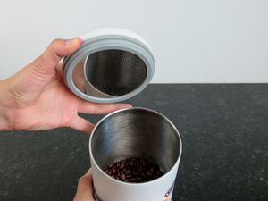 One hand holding the lid of a coffee container and the other holding the body of the container