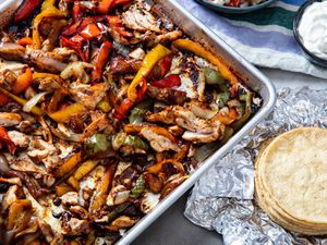 Sheet Pan chicken fajitas with a stack of tortillas nearby.