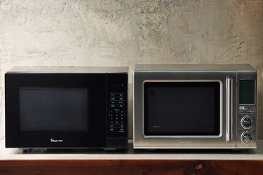 two microwaves on a wooden surface with gray background.