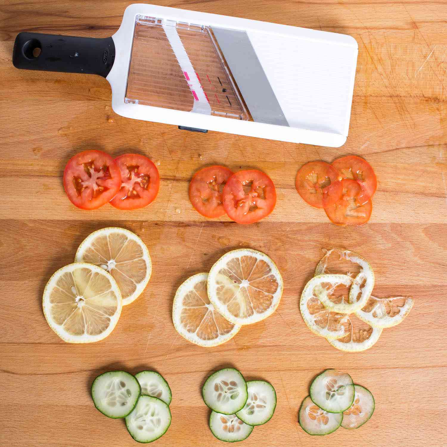 Slices of tomato, lemon, and cucumber next to the handheld mandoline