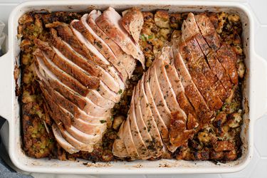 Sliced, herb-roasted turkey breast on top of stuffing inside of a white stoneware baking dish.