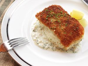 A piece of pan-seared fish with a crispy crumb coating on top, sprinkled with chopped herbs.