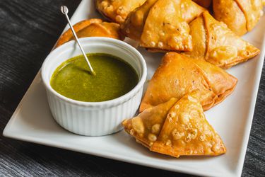 Samosas on a serving plate with a ramekin of herb chutney alongside