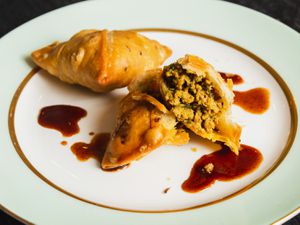 Two kheema samosas on a plate, one broken open to show its interior