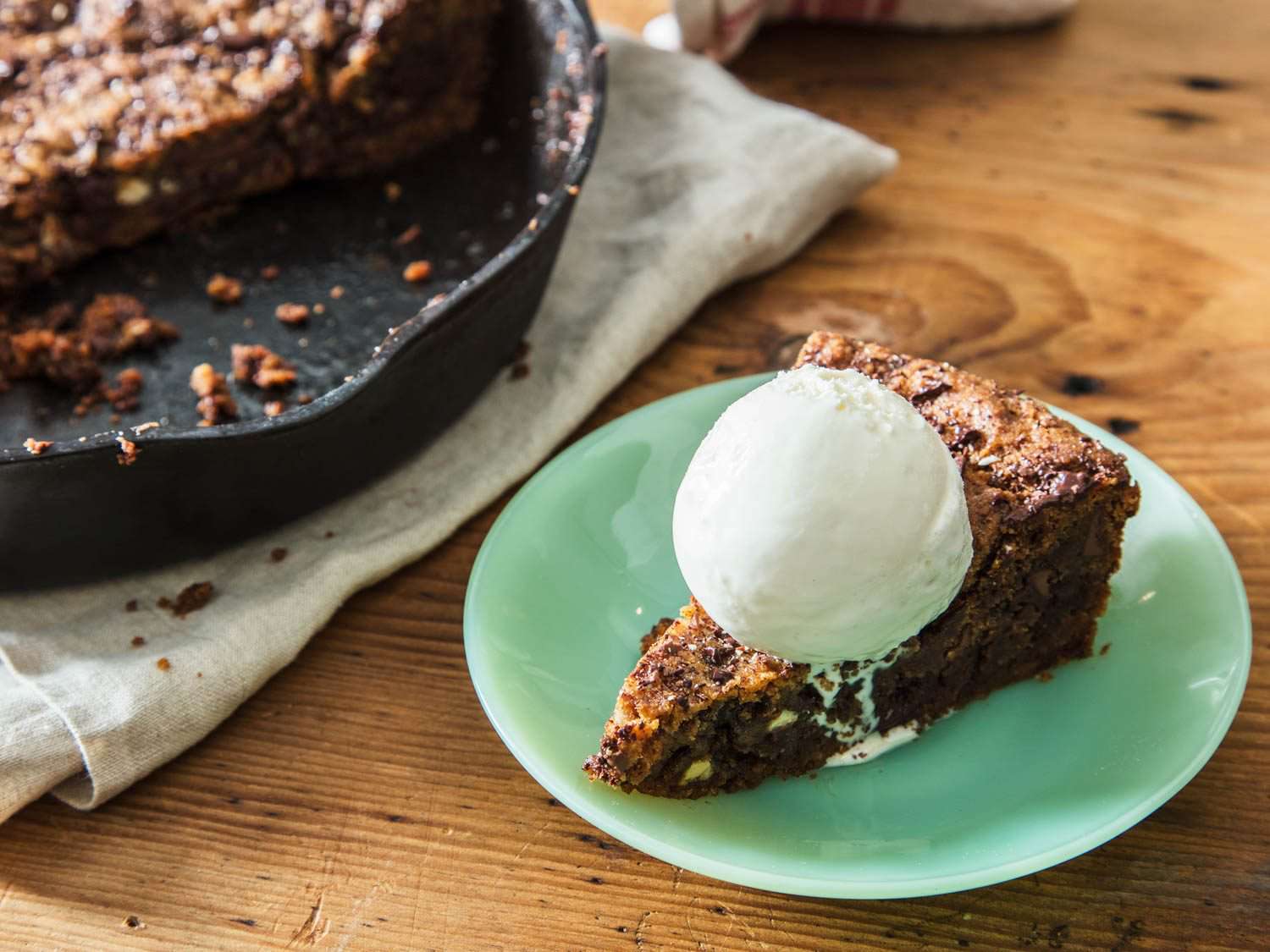 Close-up of a plated slice of the skillet cookie, topped with a scoop of vanilla ice cream.