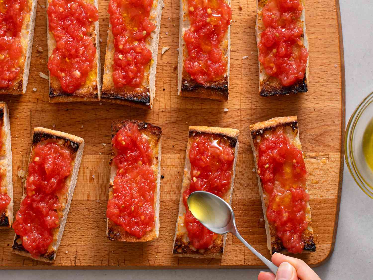 The pan con tomate being drizzled with olive oil from a spoon.