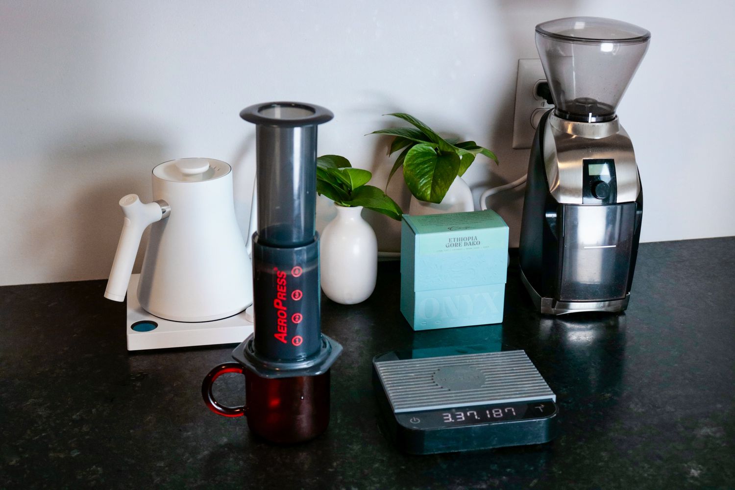 黑色台面上的压机，背景是咖啡研磨机和水壶。