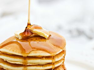 A stack of pancakes with butter on top and syrup being poured over them.