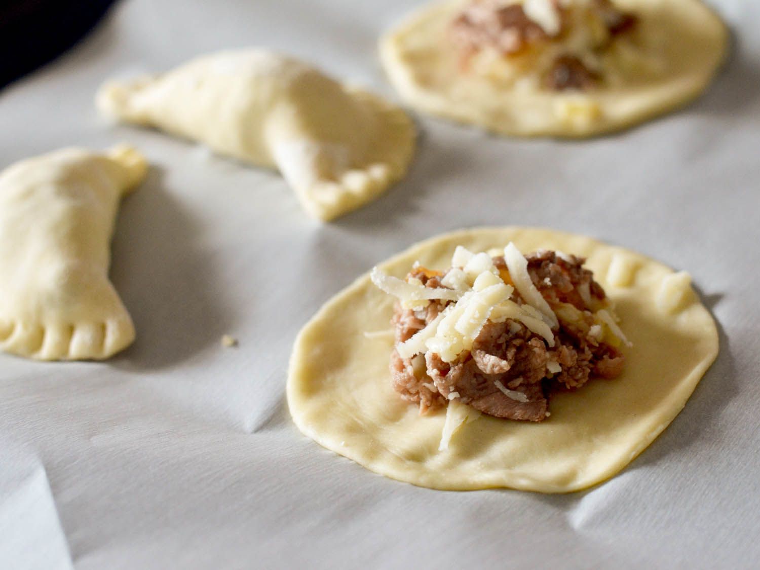 奶酪牛肉pierogi包在擀好的面团上，马上就要收口了。