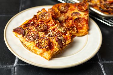 Two square slices of Sicilian pepperoni pizza on a cream colored stoneware plate.
