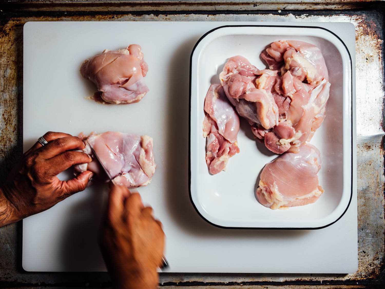 Overhead view of author scoring chicken thighs and transferring them to a baking dish.