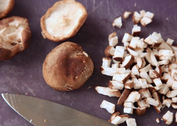 切成丁的香菇堆在砧板上，旁边是有茎的香菇帽和刀片。
