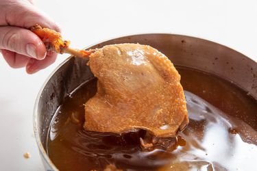 A leg of koji duck confit is held above the surface of the duck fat it was cooked in.